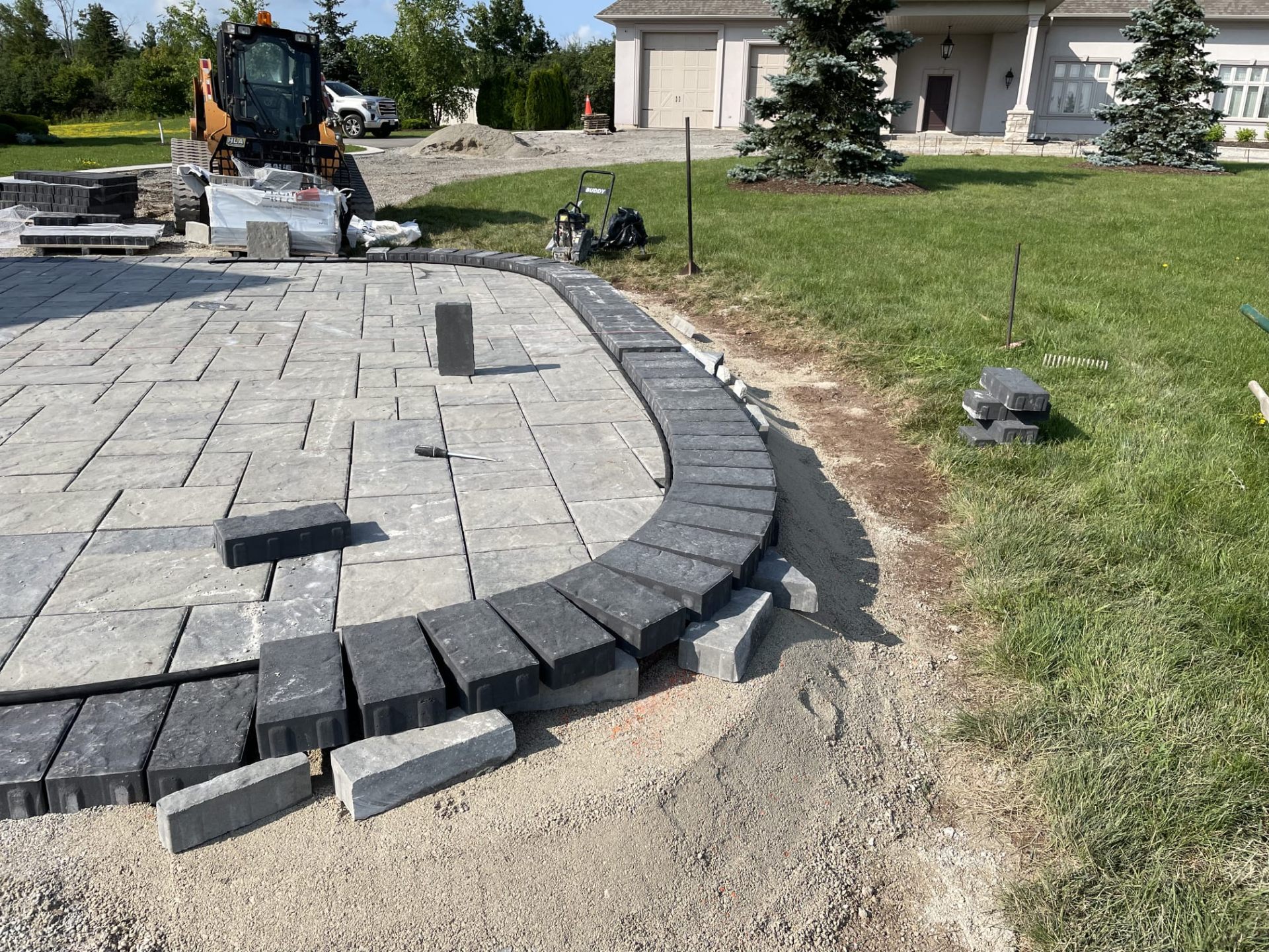 Curved charcoal soldier-course border being set on a large paver driveway apron